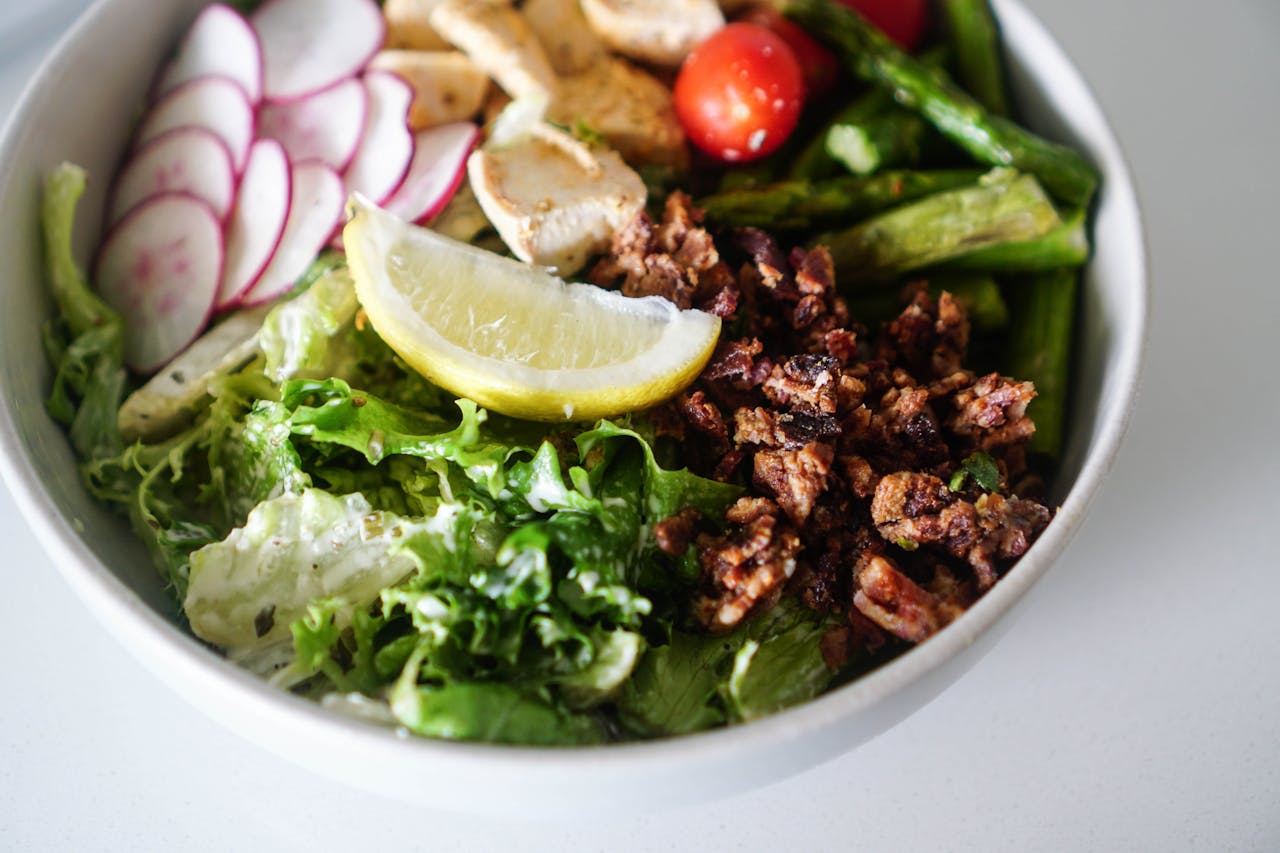 who-we-are Delicious and vibrant salad bowl featuring fresh greens, chicken, and lemon slice.